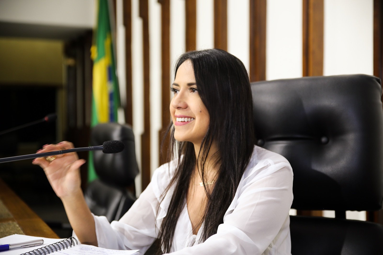 Talita Oliveira trabalhando no gabinete, ao lado da bandeira do Brasil