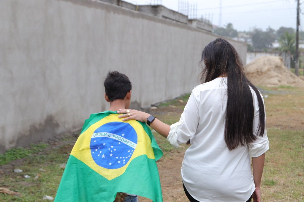 Talita Oliveira caminha de mãos no ombro de um menino enrolado na bandeira do Brasil